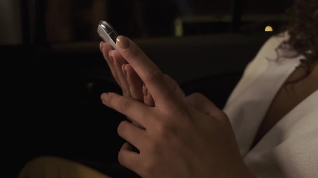 Beautiful Afro American woman tourist traveling in a taxi and rewritten with your friends on your phone at night.  Passenger Girl looking at cellphone at night in the back seat of a car.