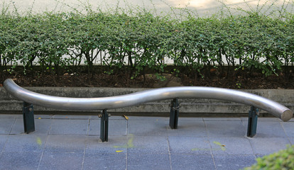 Modern metal bench at bus stop against leaf wall