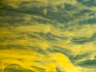 Abstract flows of yellow paint in water, close up view. Blurred background. Droplet of acrylic ink dissolving into water, abstract pattern. Ink mixing with liquid, abstract background