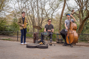 A Jazz trio featuring alto saxophone, standup bass, and drums plays in New York City's Central Park...