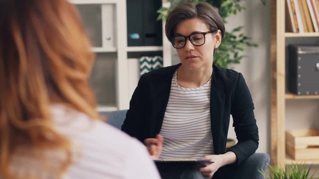 Successful therapist is discussing problems with female client sitting in office together talking and gesturing. Occupation, psychology and conversation concept.
