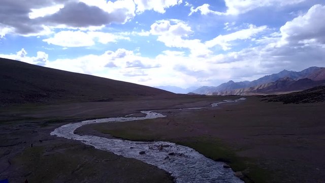 Aerial shot over the Ladakh Trek at high altitude as a river flows on the plain, man wondering over the horizon