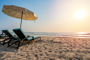 Sun umbrellas and chairs on tropical beach with sunset