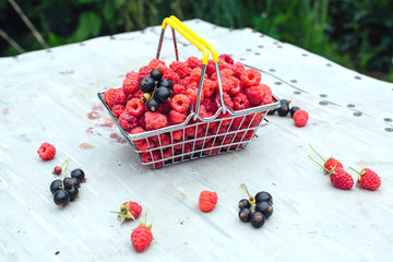 Mini shopping basket full of fresh red ripe raspberry and blackberry on vintage background
