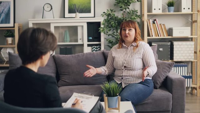 Unhappy overweight lady is opening up to professional psychologist in modern office talking and gesturing describing problems. Psychology and healthcare concept.