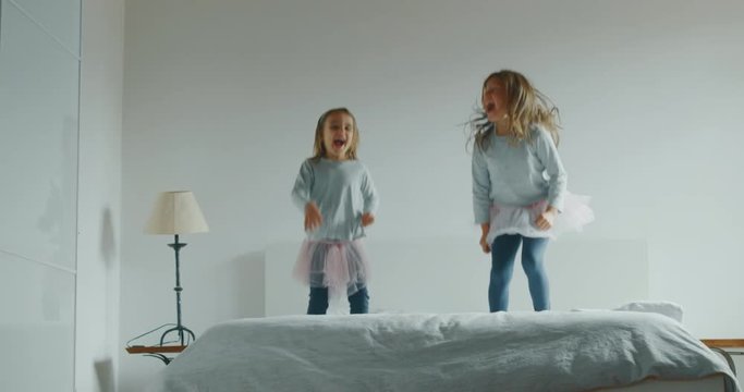 Authentic shot of two little girls sisters in pigiama and pink tutu having fun jumping on the bed of their parents bedroom.