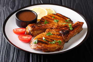 Serving grilled pork cutlet with tamarind sauce, lemon and fresh tomatoes close-up on a plate. horizontal