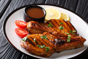 Freshly prepared grilled pork steak with tamarind sauce, lemon and fresh tomatoes close-up on a plate. horizontal