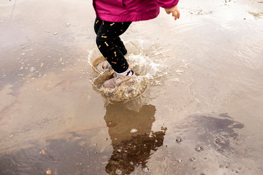A preschool aged girl playing outdoors on a rainy day with a colorful rain jacket on.