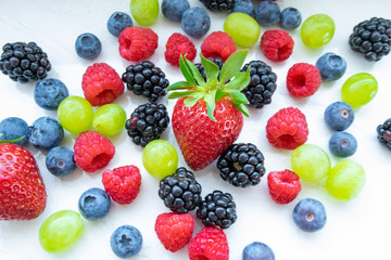 Fototapeta na wymiar bright colored fresh berries on a light background. Strawberries, blueberries, raspberries, grapes, blackberries on the table