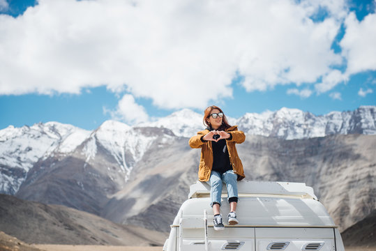 Young woman traveler in yellow jacket with heart shape enjoying beautiful mountain sitting on the car roof.