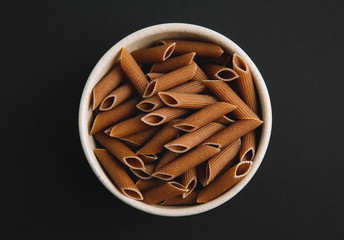 Whole grain macaroni on dark background, top view, free space for text