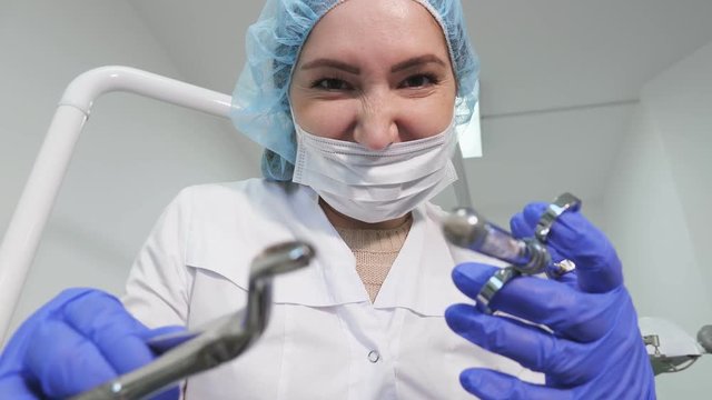 Portrait of dentist woman doctor in uniform is holding dental instruments forceps and needle in hands, patient point of view.
