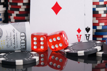 two red dice, surrounded by a gambling set of dollars, cards, casino chips, on a black background