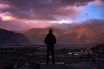 Man standing on a rock, enjoying the beautiful sunset over a valley in nubra valley, leh, ladakh, india.