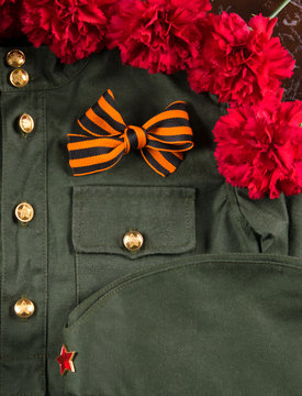 on the background of the monument, a bouquet of red carnations, military uniform with a Gergiev ribbon in the form of a bow