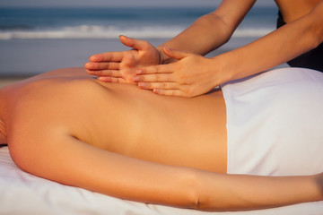 portrait of young beautiful woman on massage table beach morning getting spa on bach and sholders