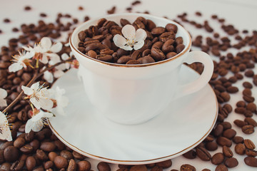  A white cup and saucer filled with coffee beans. On a white background coffee beans