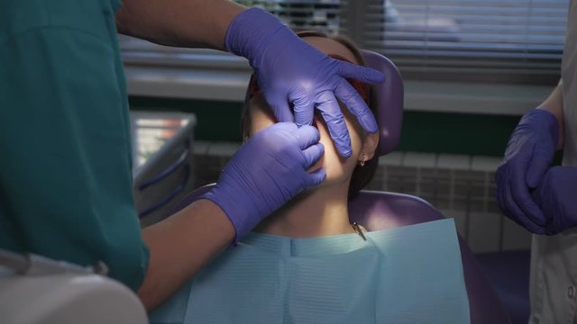 Dentist is taking care about patient's tooth with black cavity on it using electric dental brush. Nurse with saliva ejector near the patient is helping to doctor. Woman's portrait in dental chair.