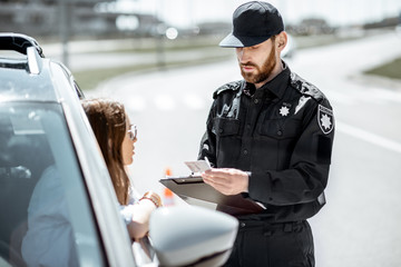 Policeman checking documents of a young female driver standing near the car on the roadside in the city