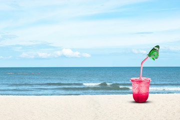 Green Butterfly on Red juice with ice in a plastic glass Background sea and the bright sky.