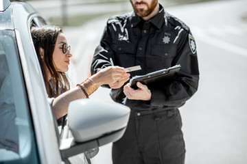 Policeman checking documents of a young female driver standing near the car on the roadside in the city