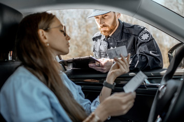Policeman checking documents of a young female driver sitting in the car, view from the car interior