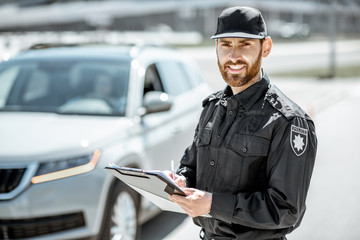 Portrait of a handsome policeman in uniform standing in front of a car on the roadside