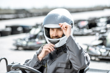 Portrait of a professional racer in sportswear and helmet sitting in the kart on the track