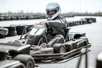 Racer in sportswear and protective helmet driving go-kart on the track