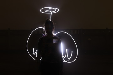 woman in the image of an angel with painted light wings on a black background.