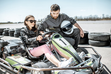 Man in sportswear instructing young woman driver before racing on the go-karts on the track outdoors - obrazy, fototapety, plakaty