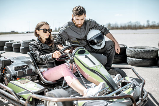 Man In Sportswear Instructing Young Woman Driver Before Racing On The Go-karts On The Track Outdoors