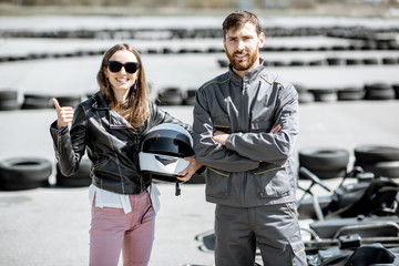 Happy instructor in sportswear with young woman driver on the go-kart track outdoors - obrazy, fototapety, plakaty