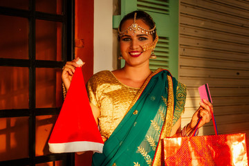 happy beautiful indian female person in traditional dress holding shop bag and Santa Claus hat in market,shopping bags and credit card.black friday sales