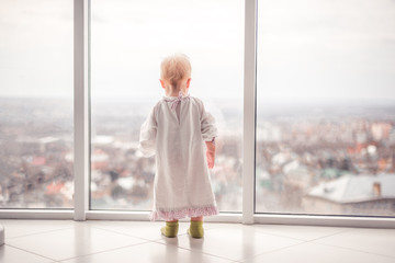 Pretty child with a blond hair looking at the large window