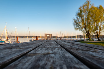 Fototapeta premium wooden table against a littel harbour at a lake at sunset, shaloow depth of field