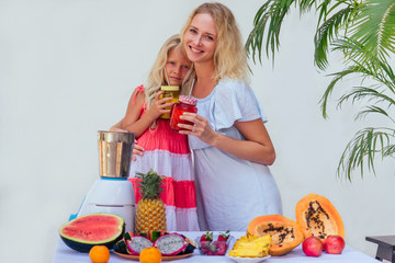 caucasian family in the kitchen during breakfast at home. two blonde sisters cooking smoothies in a blender.tropical summer theme