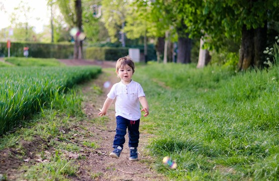 Cute happy funny little baby boy running on dirt road with green grass trying to catch soap bubbles. Childhood emotions