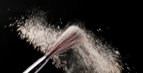 Fine art cosmetic, makeup concept with a highlighted soft bristle brush and a puff of facial powder on a black background with copy space for your text
