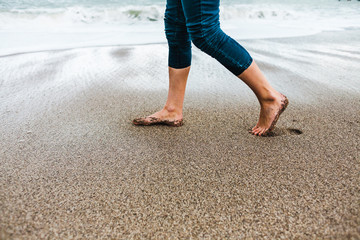 Barefoot girl in jeans walking along the sandy shore.