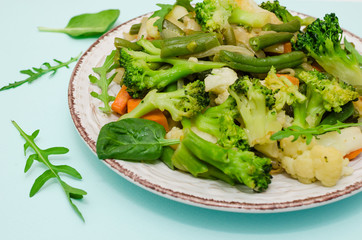 Vegetable stew in the plate on blue background. Carrots, green beans, broccoli and zucchini. Fresh green vegetables. Close up. Health food