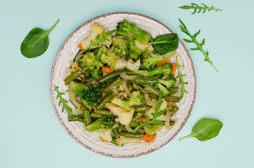 Vegetable stew in the plate on blue background. Carrots, green beans, broccoli and zucchini. Fresh green vegetables. Close up. Health food