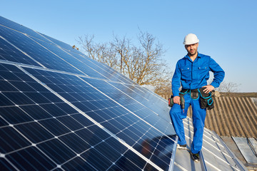 Smiling engineer in blue suit and protective helmet installing solar photovoltaic panel system...