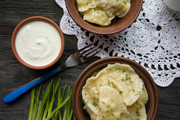 Dumplings with potatoes and cabbage. Sour cream, milk and greens. Traditional dish of Ukraine. Dark wooden background.