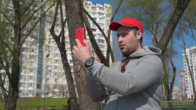 Funny man in red cap makes selfie on smartphone. Man makes photos on mobile phone, take a pictures
