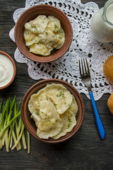 Dumplings with potatoes and cabbage. Sour cream, milk and greens. Traditional dish of Ukraine. Dark wooden background.