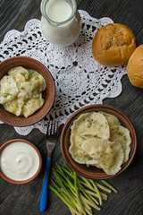 Dumplings with potatoes and cabbage. Sour cream, milk and greens. Traditional dish of Ukraine. Dark wooden background.
