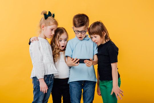 a group of young children, saw what they should not see on the smartphone, isolated yellow background, copy space