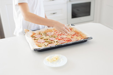 Cooking concept - cook manually adding grated cheese to pizza in the home kitchen. Close-up